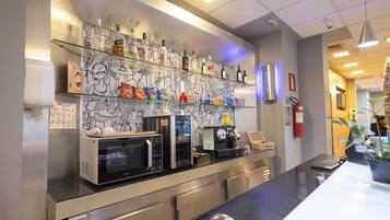 Un área de cocina con microondas, cafetera y refrigerador. Hay estantes con condimentos y bocadillos.