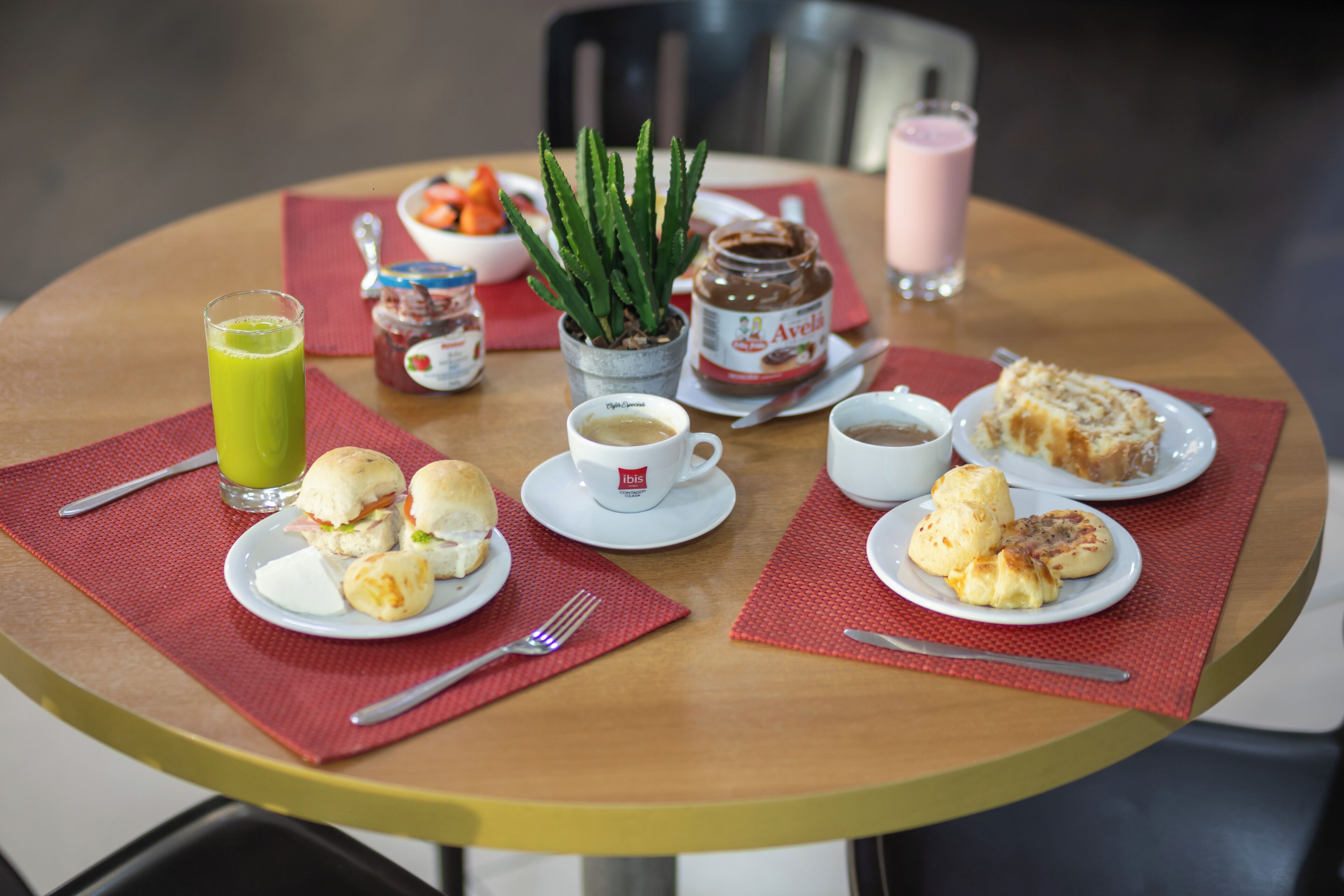 Una mesa de desayuno con diversas opciones de comida, incluyendo pastelería, una planta y un frasco de mermelada.