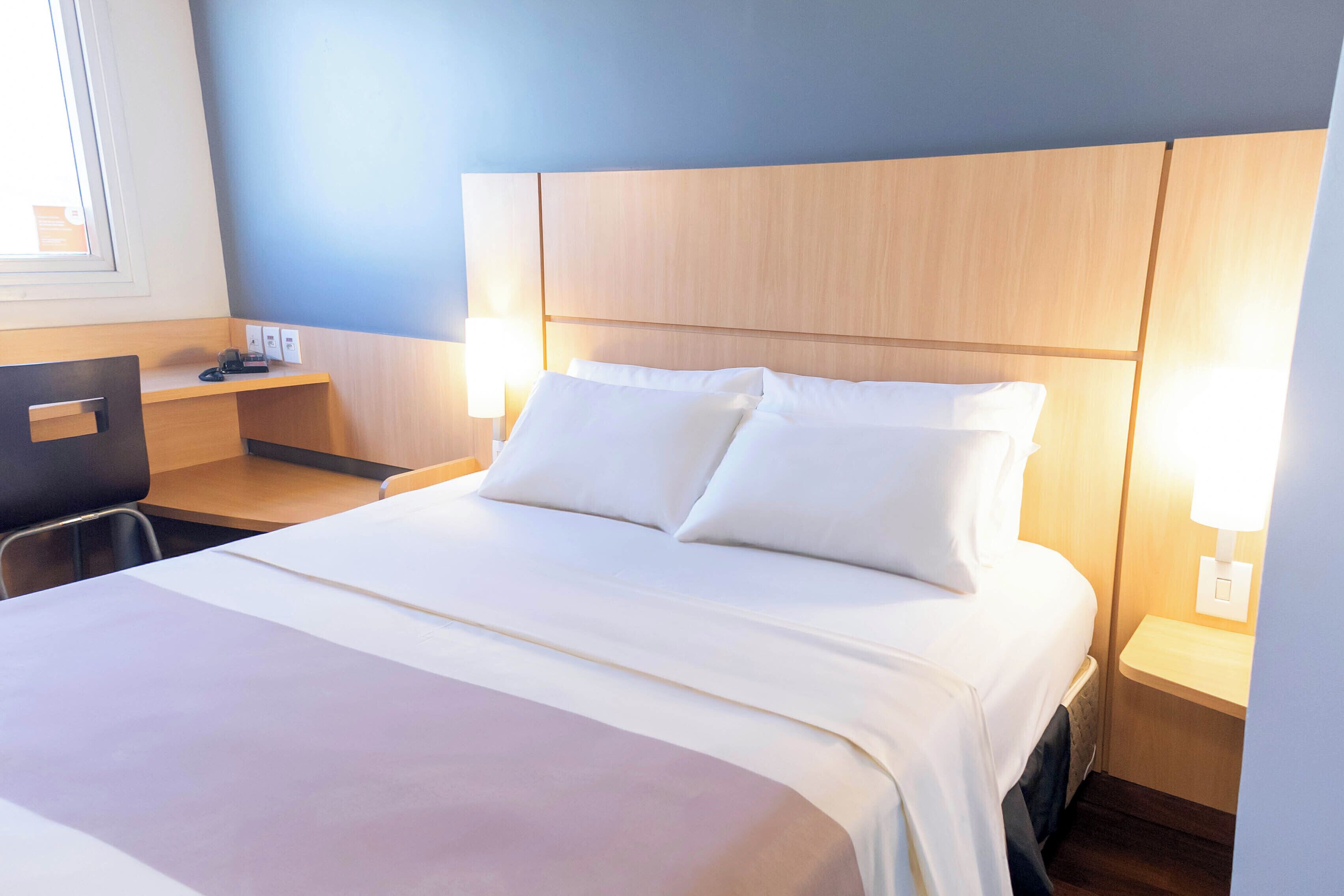 Et hotelværelse med seng, sengeborde, et skrivebord og en stol.