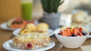 Uma mesa com diversos alimentos, incluindo um pastel com coco ralado, uma tigela de frutas vermelhas e outros pratos ao fundo.