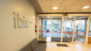Zona de recepción con un sofá, un cartel que dice 'ibis Contagem' y un acceso por puerta de vidrio.