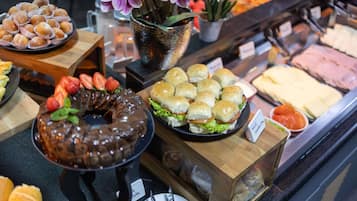 Un bufé con diferentes opciones de comida, como un pastel de chocolate, sándwiches pequeños y una variedad de otros platos.