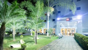 Entrada de un hotel con un camino empedrado, palmeras y un edificio con un cartel que dice 'IDIS'.