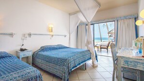 A hotel room with two beds, a balcony with a view of the beach, and a table with a vase of flowers. - Turtle Bay Beach Club (Watamu)