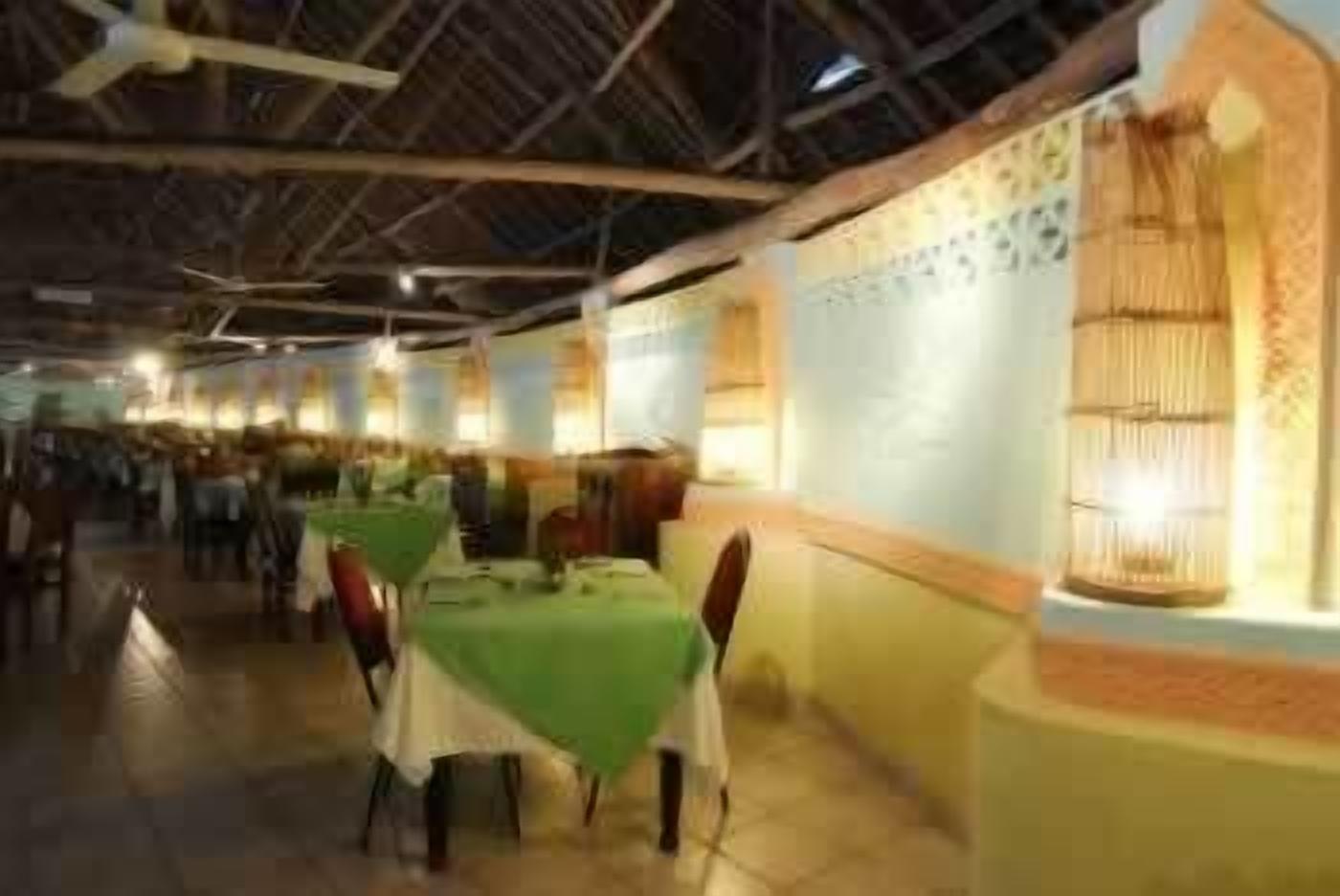Ein Restaurant mit Tischen, die mit grünen Tischdecken bedeckt sind, einer hohen Decke mit freiliegenden Balken und traditioneller Wandgestaltung.