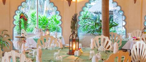 A dining area with tables set for a meal, featuring white chairs and a green tablecloth.