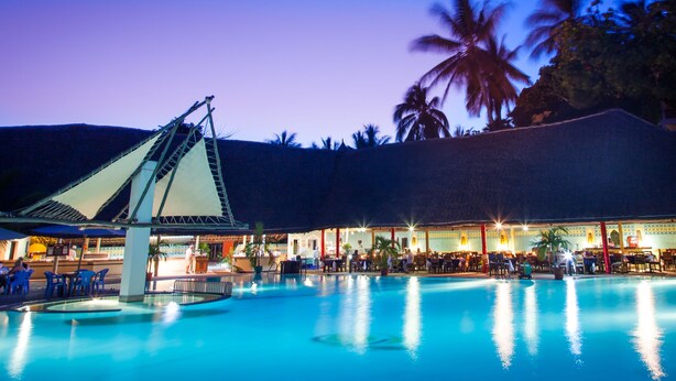 A pool area with a covered seating area and palm trees in the background. - Turtle Bay Beach Club (Watamu)