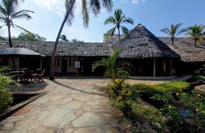 A courtyard with thatched-roof huts, stone flooring, and tropical plants. - Turtle Bay Beach Club (Watamu)