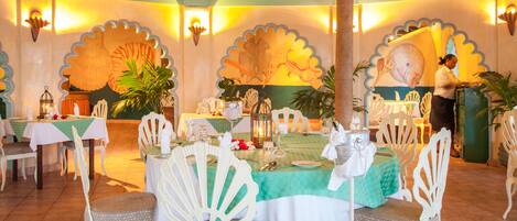 A dining area with round tables, white chairs, and a tropical theme.