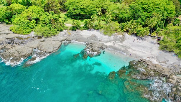 An aerial view of a beach with clear turquoise waters, rocky areas, and dense green foliage. - El Sano Banano Beachside Hotel (Cóbano)