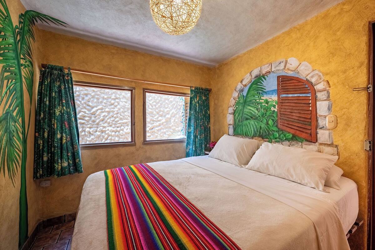 A room with a bed, two windows with curtains, a stone archway, and a textured wall.