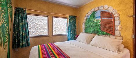 A room with a bed, two windows with curtains, a stone archway, and a textured wall.