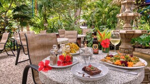 An outdoor dining area with wicker chairs, a table with plates of food, a bottle of beer, and a decorative fountain. - El Sano Banano Beachside Hotel (Cóbano)