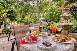 An outdoor dining area with wicker chairs, a table with plates of food, a bottle of beer, and a decorative fountain. - El Sano Banano Beachside Hotel (Cóbano)