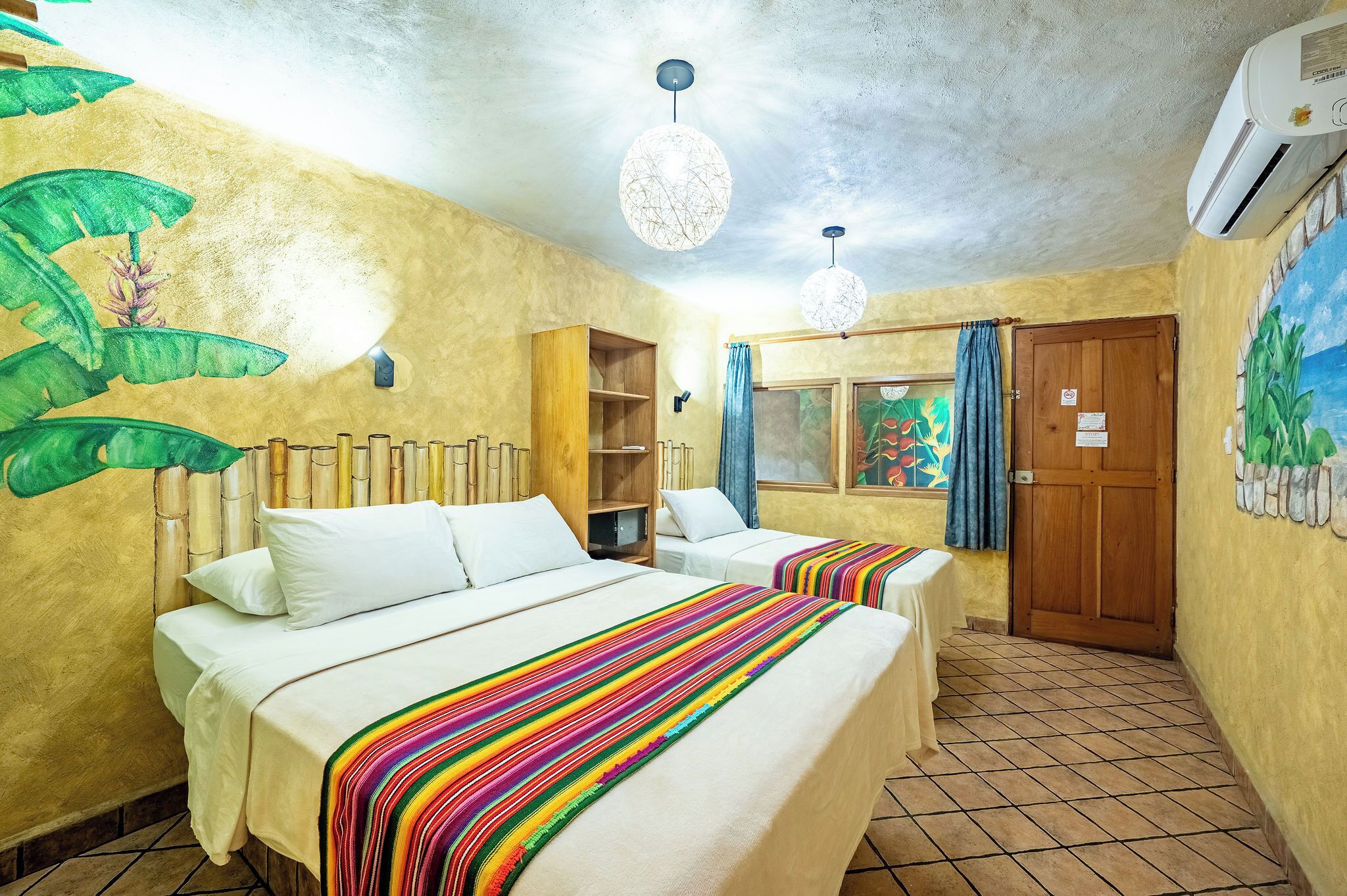 Une chambre avec deux lits, une étagère en bois, une fenêtre avec des rideaux et une fresque murale.