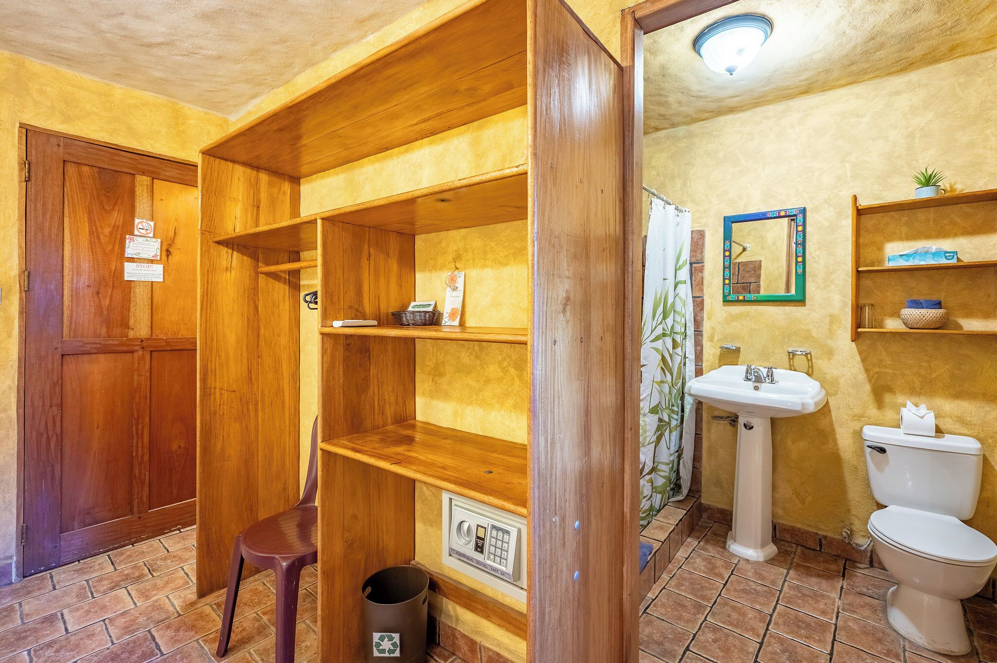 Un baño con un estante de madera, un lavabo, un inodoro y un cubo de basura.