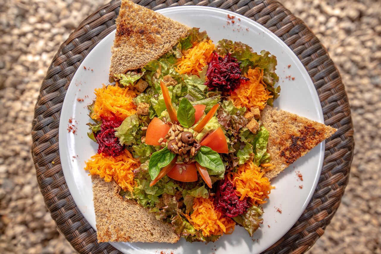 Uma salada com diversos vegetais e uma fatia de pão sobre uma cesta de palha.