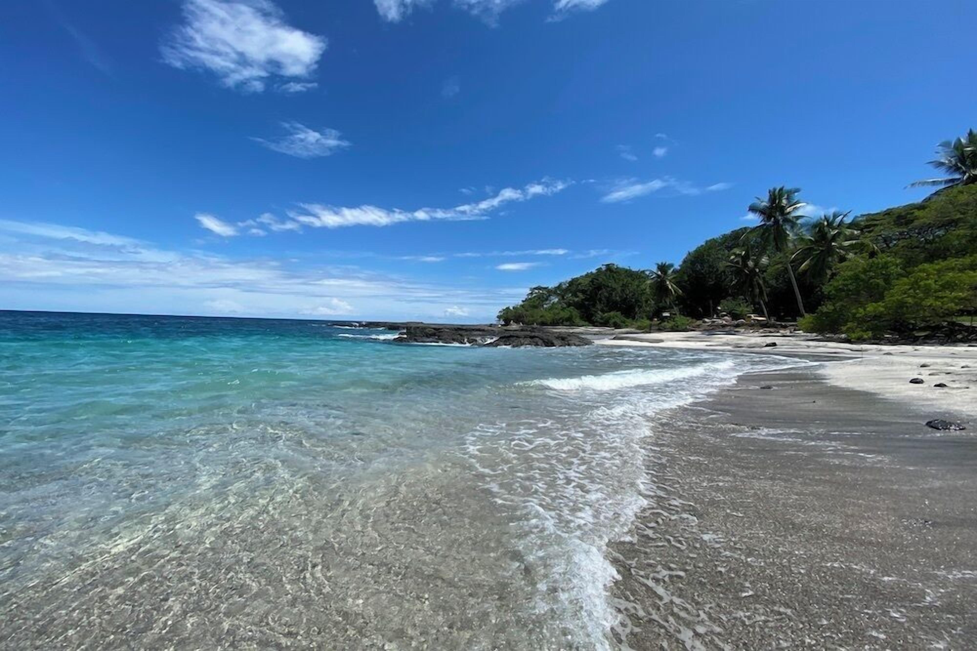 Una playa con aguas cristalinas, una orilla de arena y una colina cubierta de bosque.