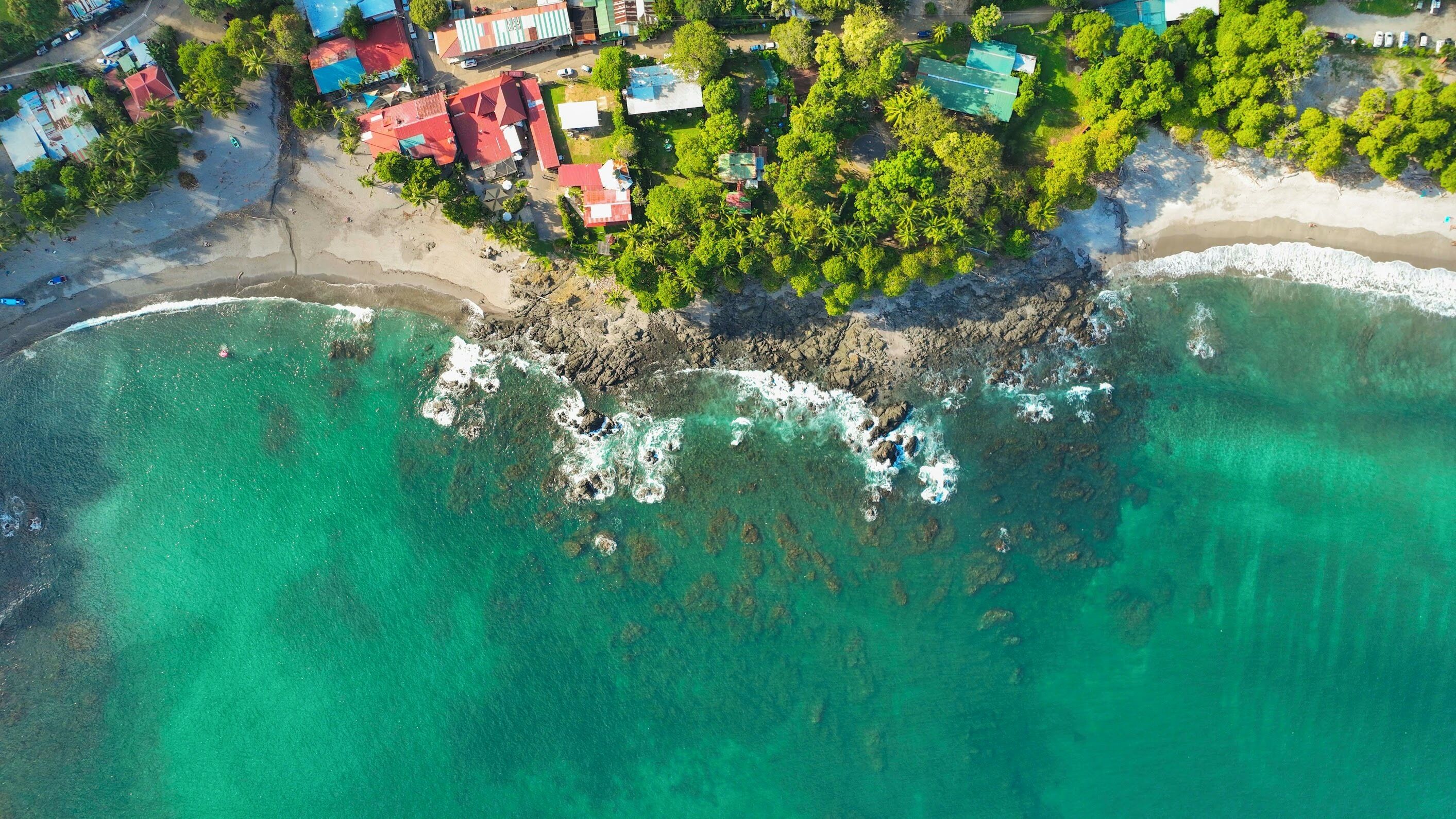 Vista aérea de una zona costera con edificios, una playa y aguas turquesas cristalinas.