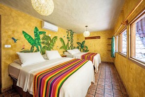 A room with two beds, a mural of tropical plants, a hanging light fixture, and a window with curtains. - El Sano Banano Beachside Hotel (Cóbano)