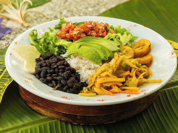 Un plato de comida con arroz, frijoles negros, aguacate, plátanos maduros y ensalada.