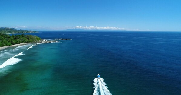 A coastal view with a boat in the foreground, clear blue ocean, and a forested coastline. - El Sano Banano Beachside Hotel (Cóbano)