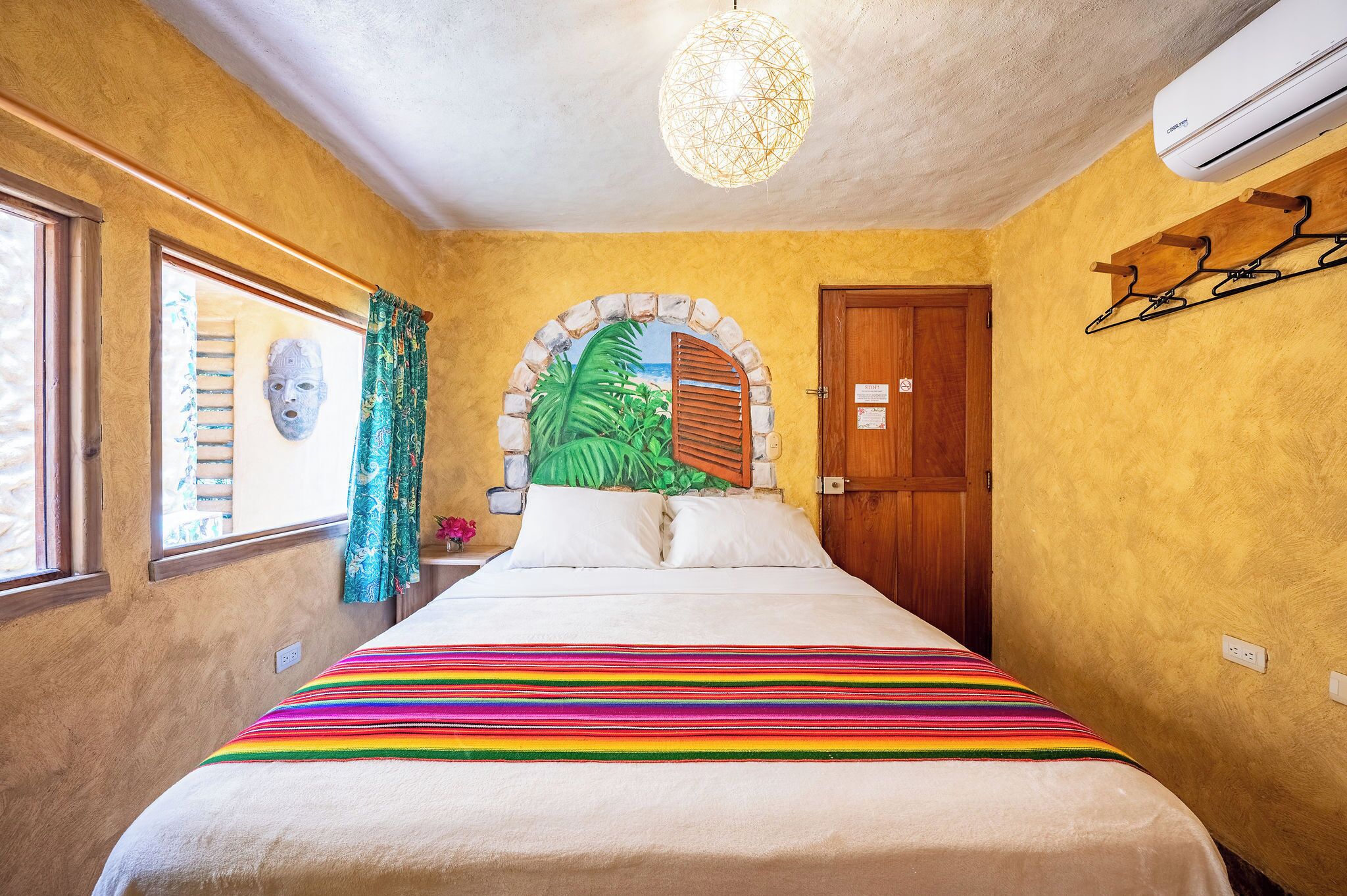 A bedroom with a bed, a window, a door, and a wall-mounted air conditioner.