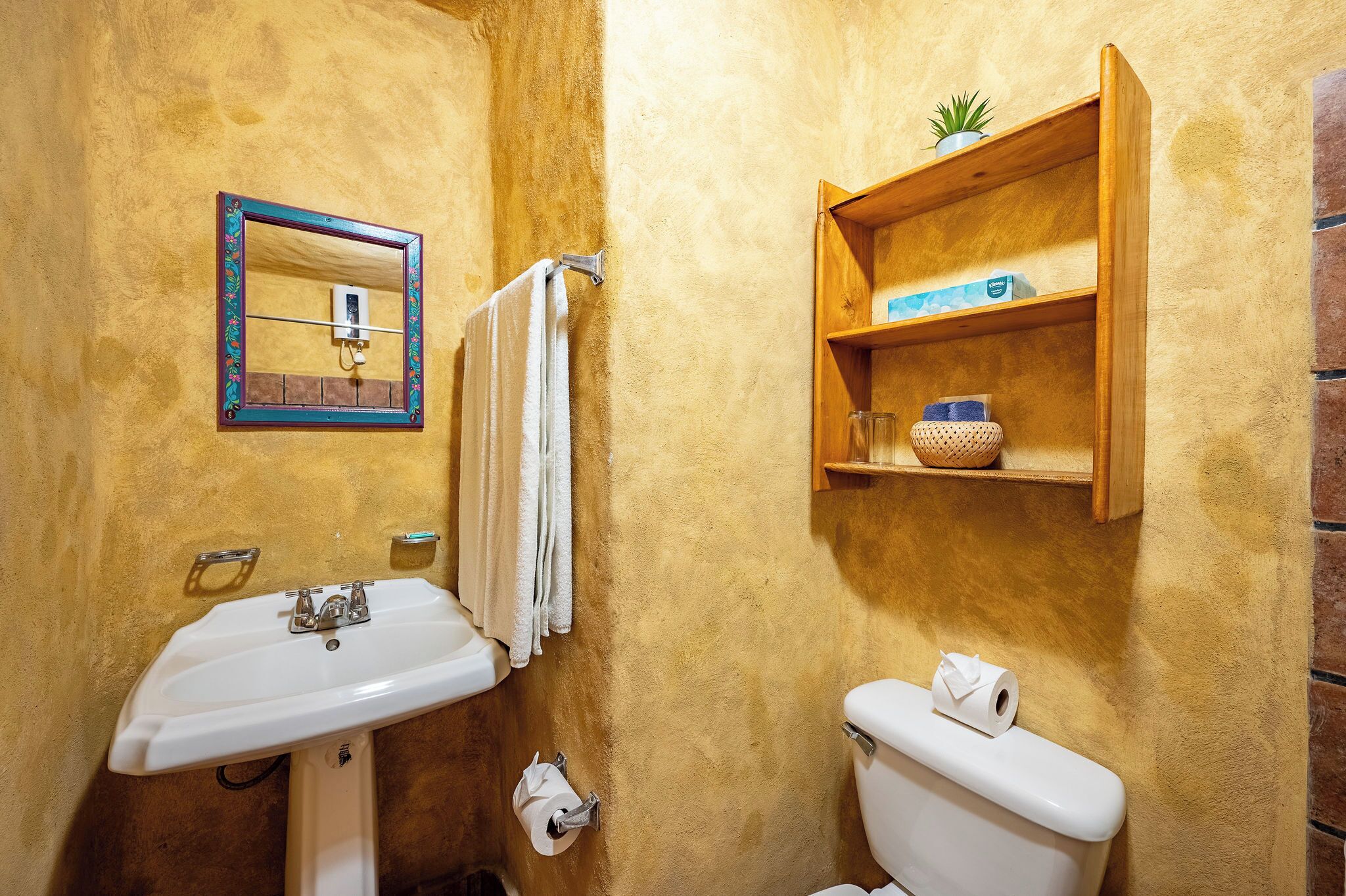 Een badkamer met een wastafel, toilet, spiegel, handdoekrek en een houten plank met toiletartikelen.