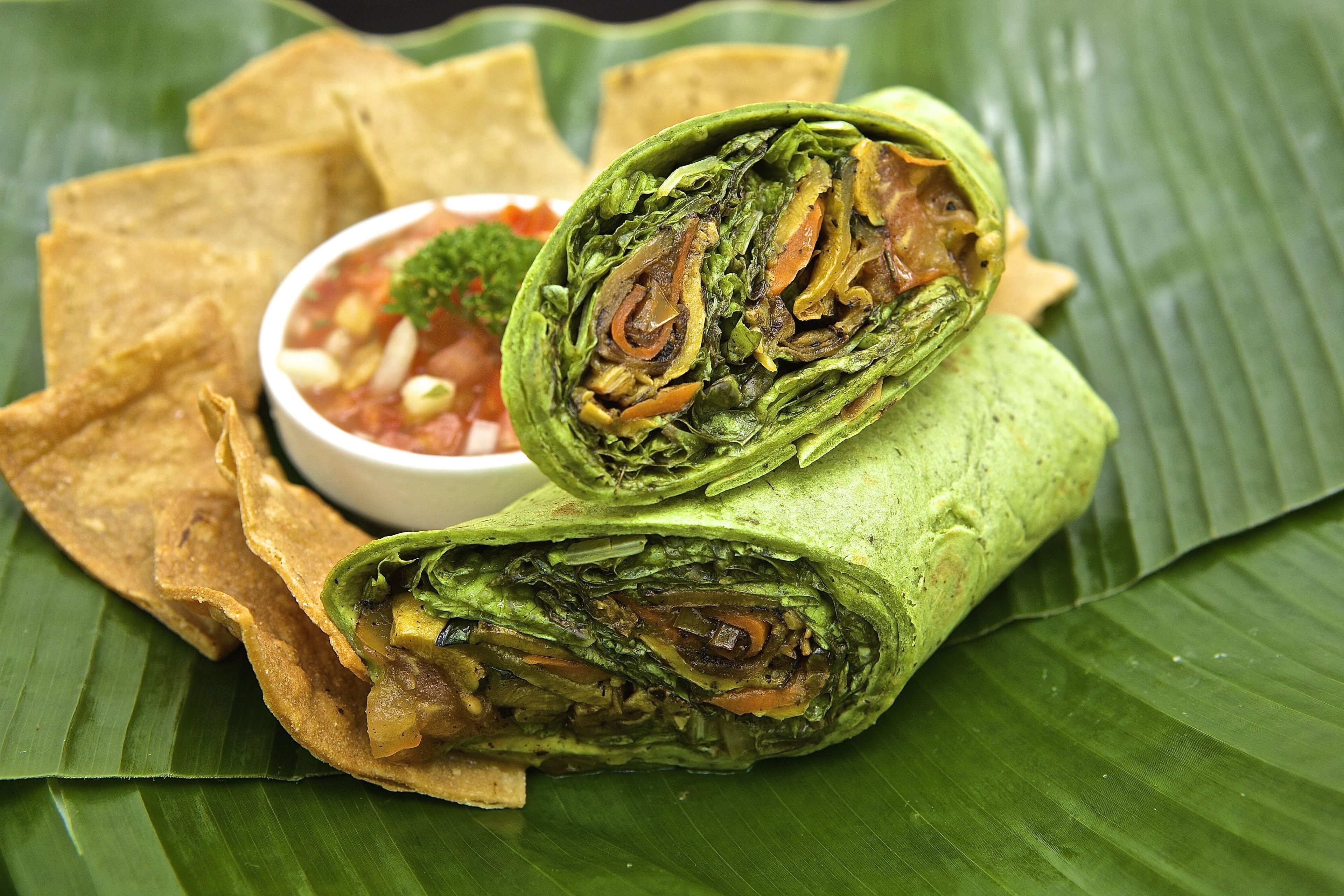 A burrito wrapped in a green leaf, served with tortilla chips and a small bowl of salsa.