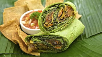 A burrito wrapped in a green leaf, served with tortilla chips and a small bowl of salsa.