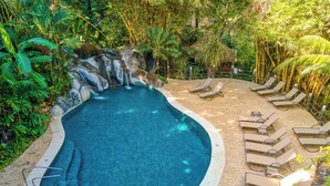 A pool with a waterfall, surrounded by lush greenery and lounge chairs. - El Sano Banano Beachside Hotel (Cóbano)