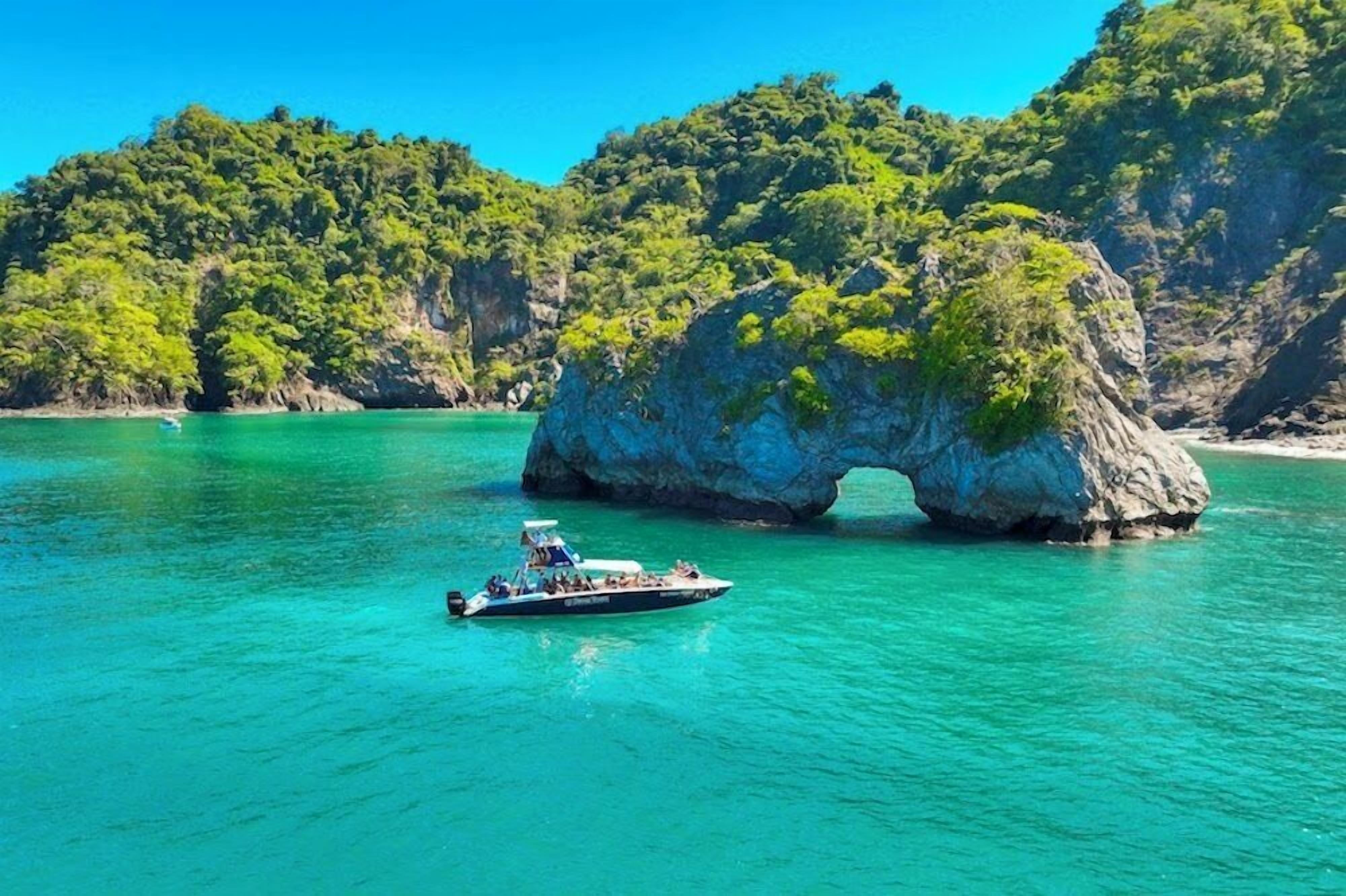 Een boot op turquoise water, met een grote rotsformatie op de achtergrond.