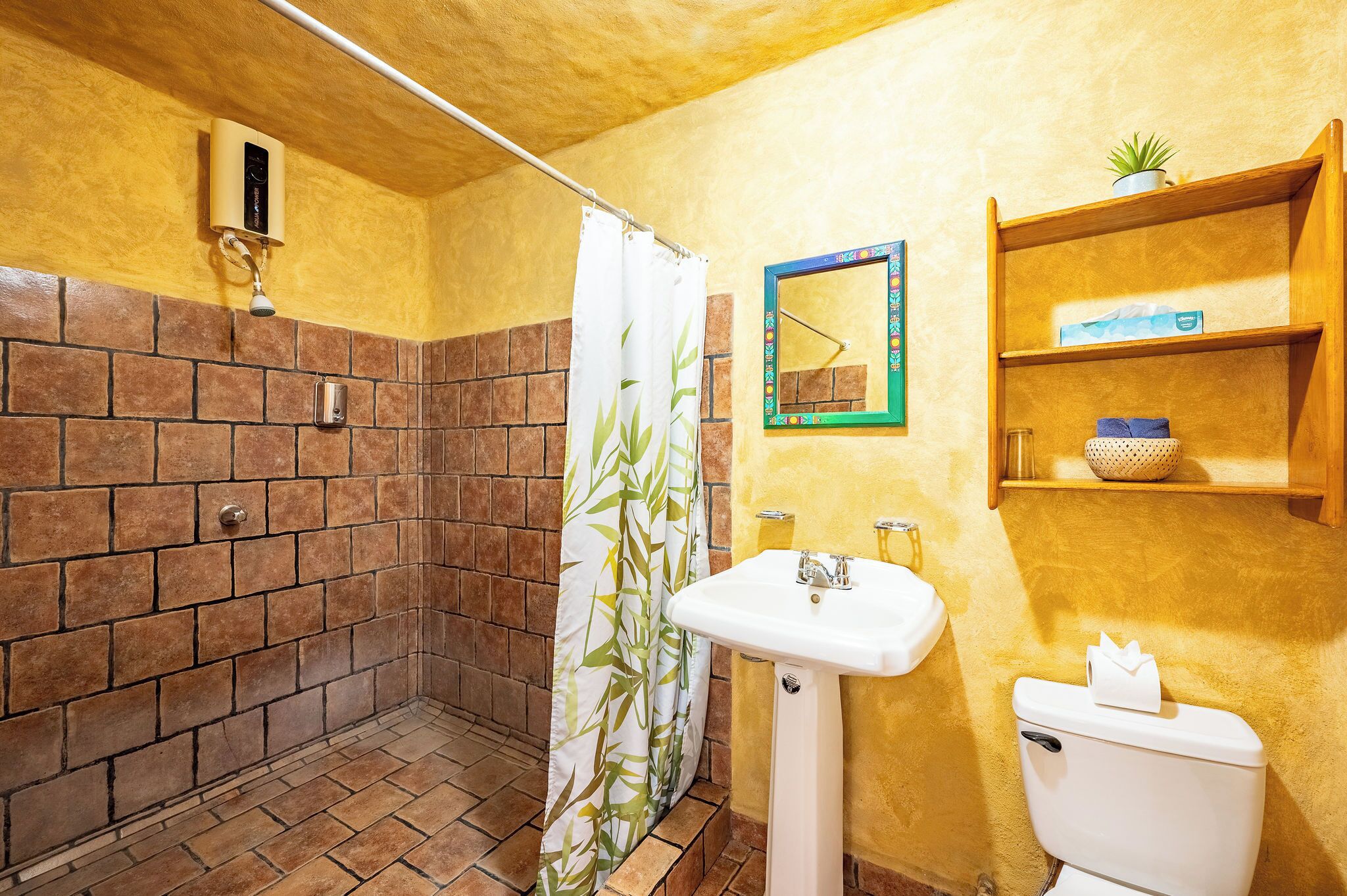 Un baño con ducha, inodoro, lavabo, espejo y repisas con artículos de aseo.