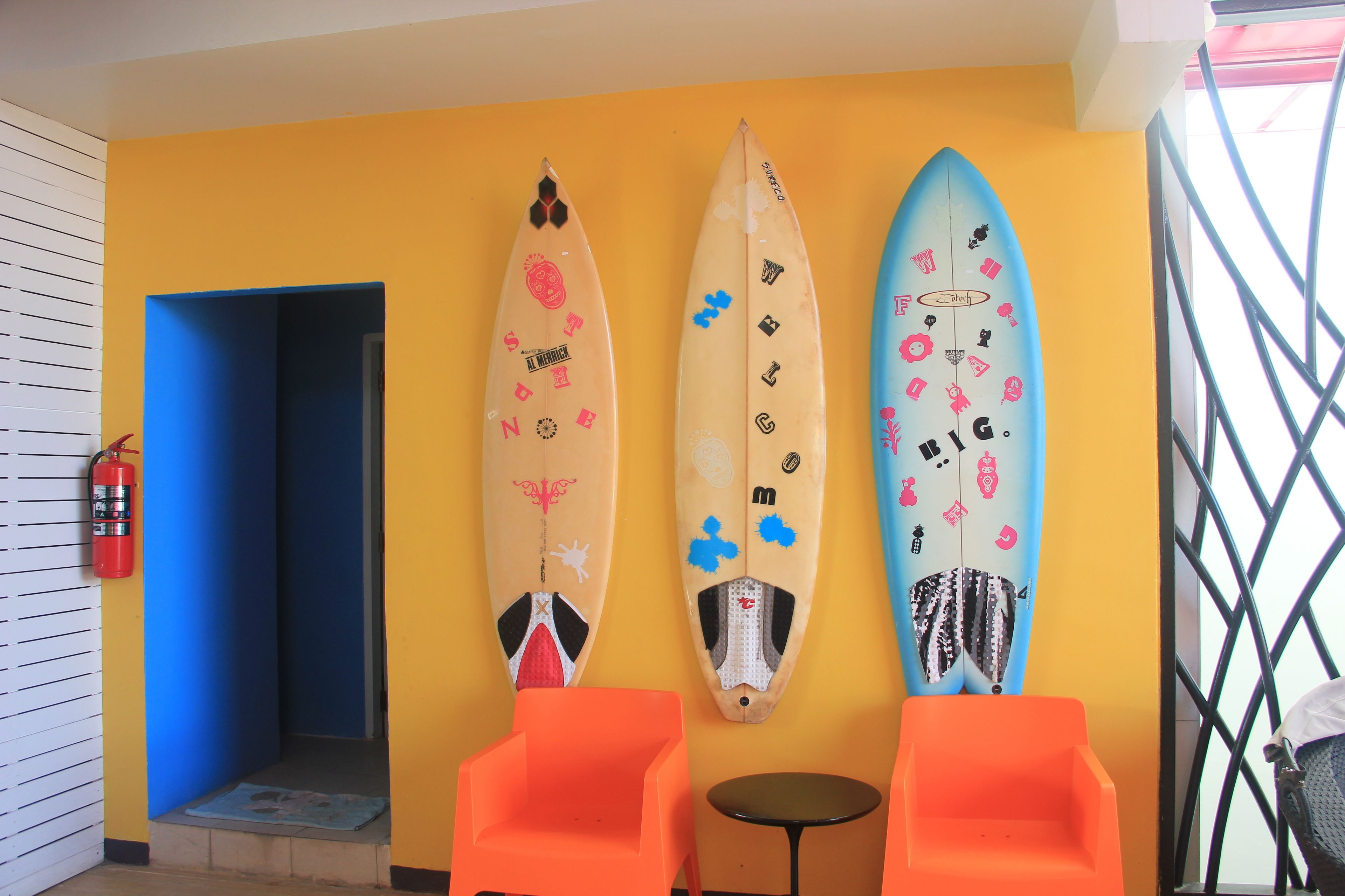 Three surfboards mounted on a yellow wall, an orange chair, and a small table.