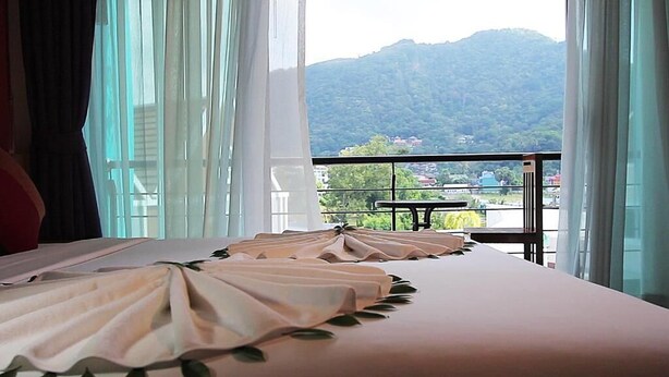 Habitación de hotel con una cama, vistas a montañas y un balcón con mesa y sillas.