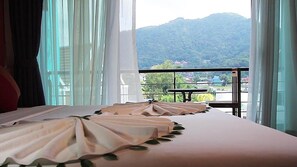 A hotel room with a bed, a view of mountains, and a balcony with a table and chairs. - Must Sea Hotel Kata (Karon)