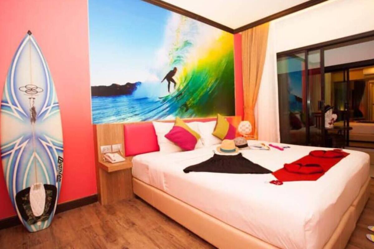 Une chambre d’hôtel avec un lit, une planche de surf et une grande fresque représentant un surfeur sur une vague.