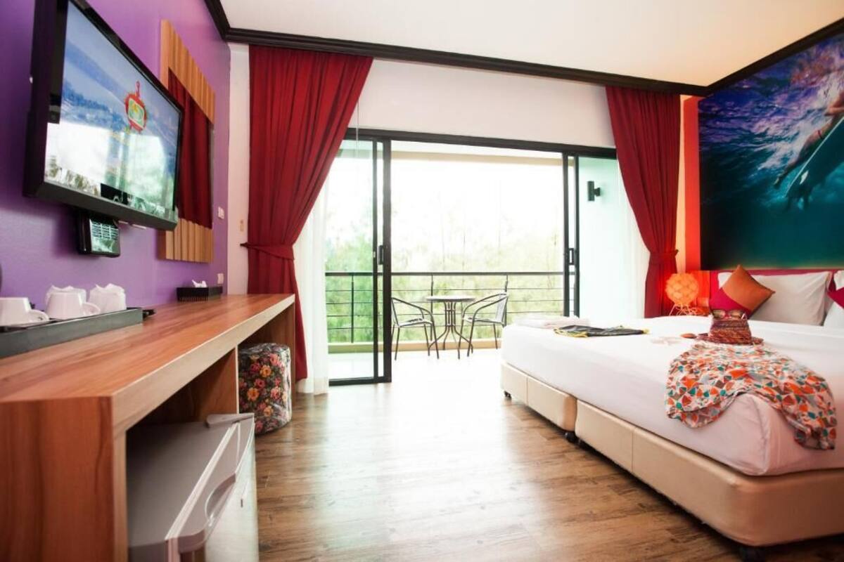 Une chambre d’hôtel comprenant un lit, un bureau avec un ordinateur, une télévision et un balcon avec une table et des chaises.