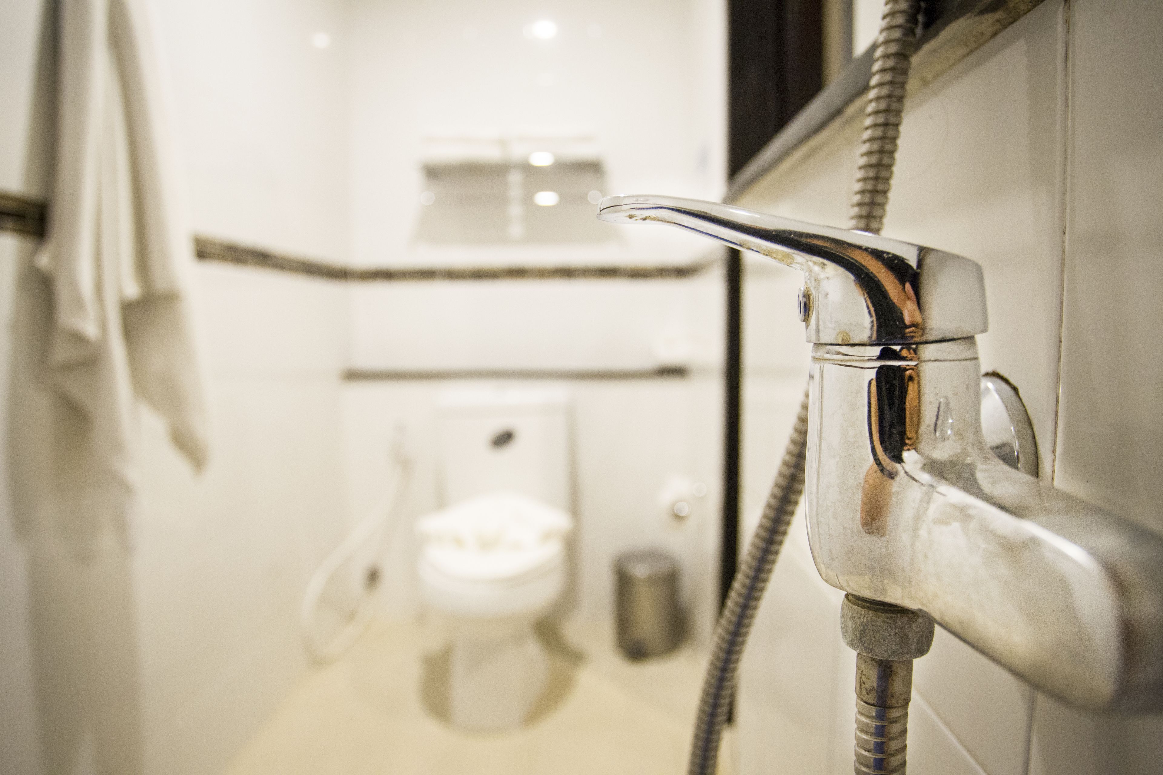 A bathroom with a modern faucet, a toilet, and a shower hose.