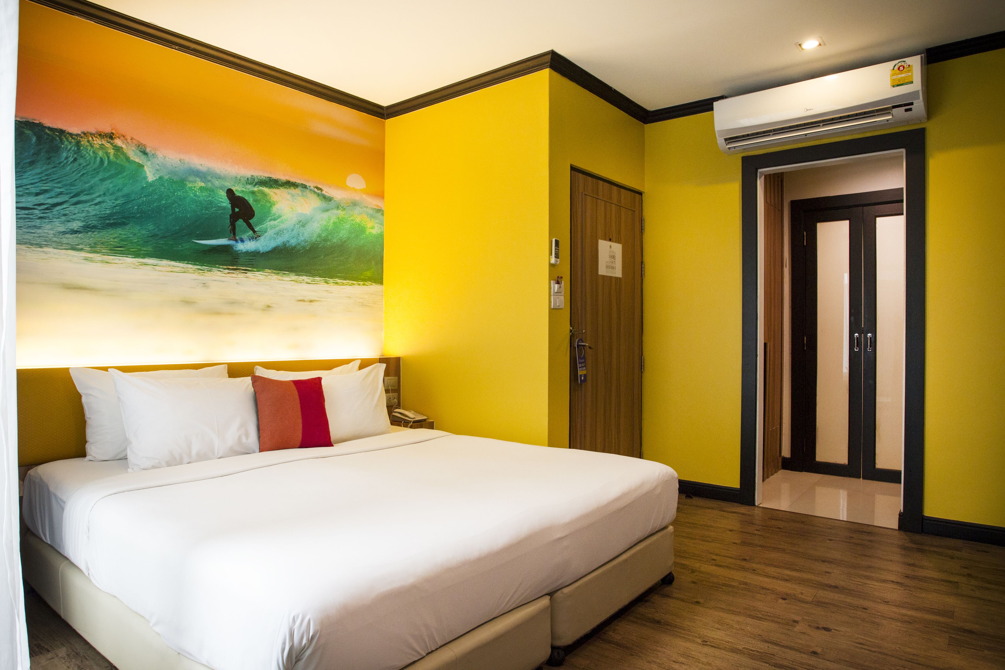 Une chambre d’hôtel avec un grand lit, un tableau représentant un surfeur sur une vague, une porte et un appareil de climatisation.
