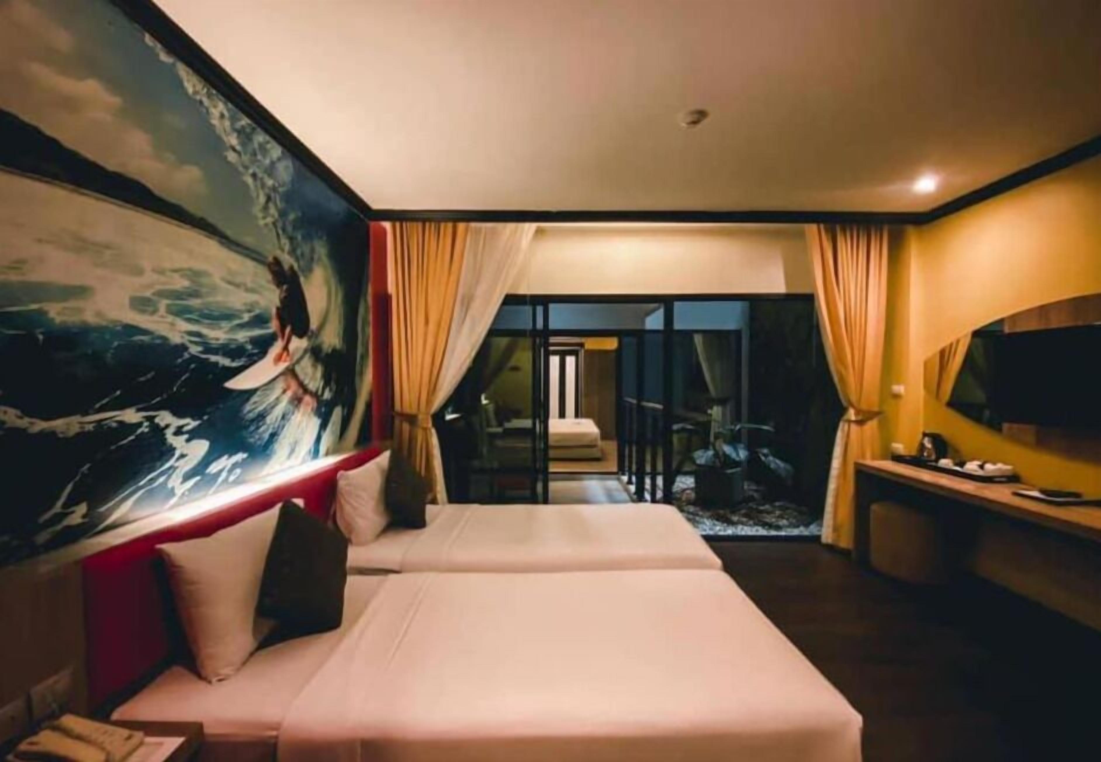 A hotel room with a large ocean-themed mural, a bed with white linens, a TV on a wooden console, and a view of the room through a glass door.