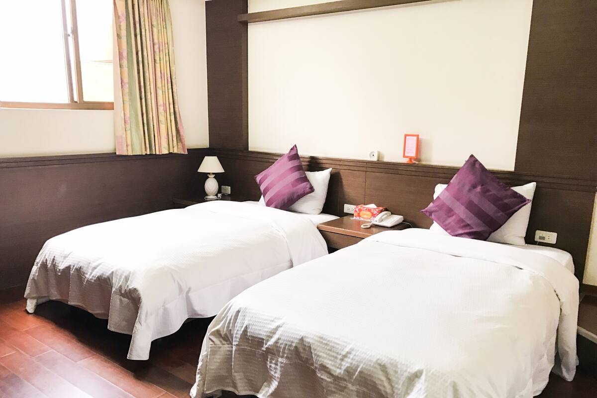 A hotel room with two single beds, a nightstand with a lamp, and a bedside table with a phone and a tissue box.