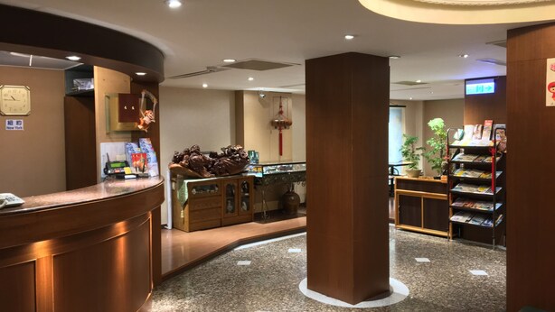 A hotel reception area with a wooden reception desk, a clock, and a display of chocolates. - FuZhuang Hotel (Taipei)