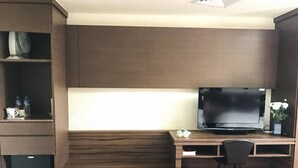 A modern office space with a wooden desk, a black chair, a television, and a small trash can. - FuZhuang Hotel (Taipei)