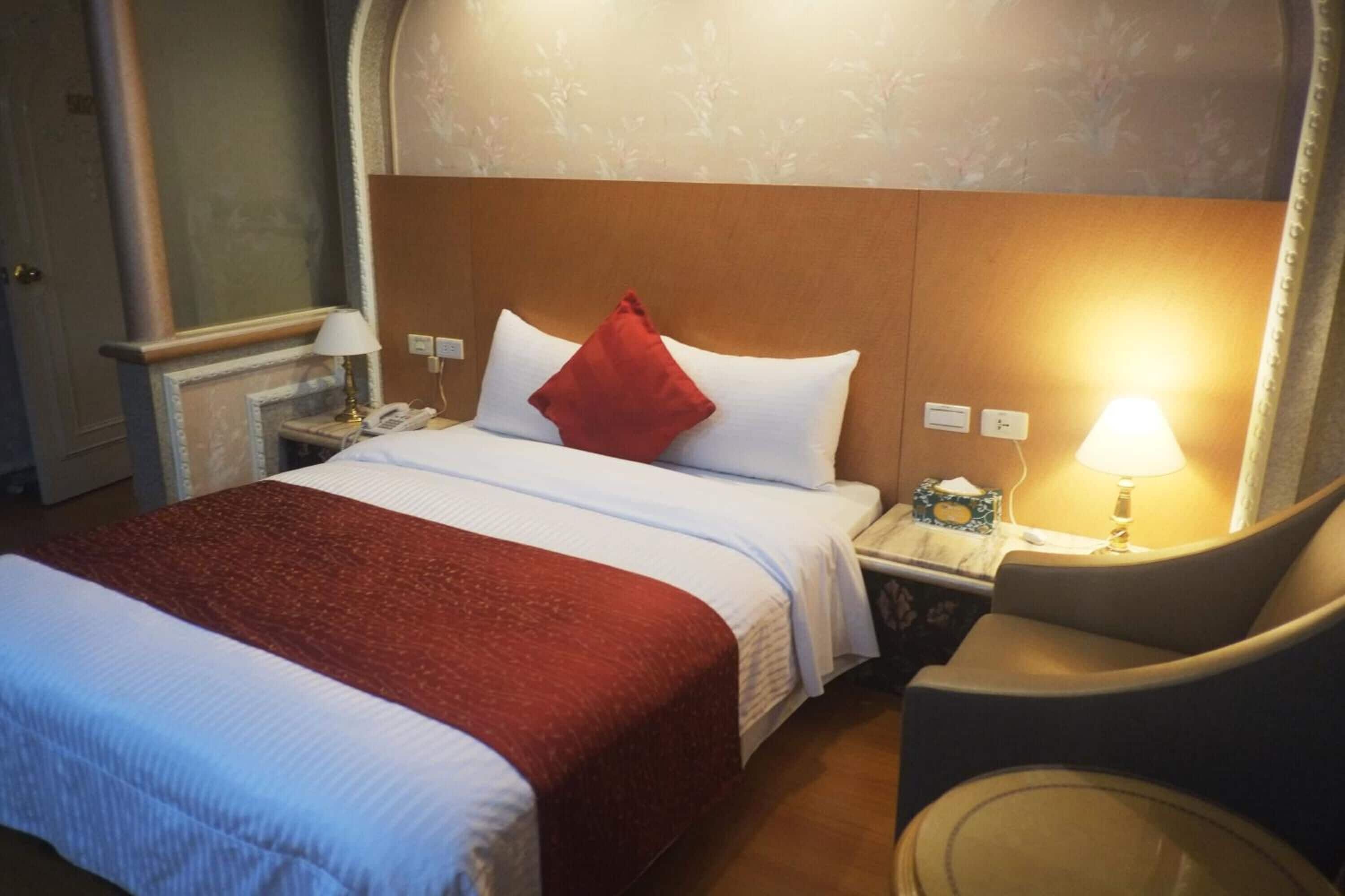 Ein Hotelzimmer mit einem großen Bett, einem Nachttisch, einem Sessel und einer Lampe.