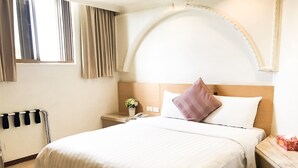 A hotel room with a large bed, a nightstand, a bedside table, a window with curtains, and a wooden headboard. - FuZhuang Hotel (Taipei)