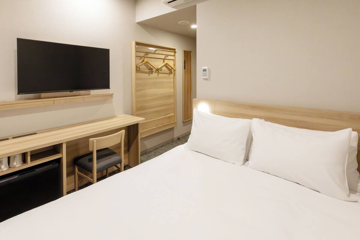 A hotel room with a bed, a desk with a chair, a television, and a wardrobe.
