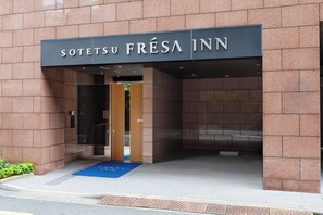 La entrada al Sotetsu Fréa Inn con un cartel sobre la puerta, un felpudo azul en la entrada y suelo de baldosas.