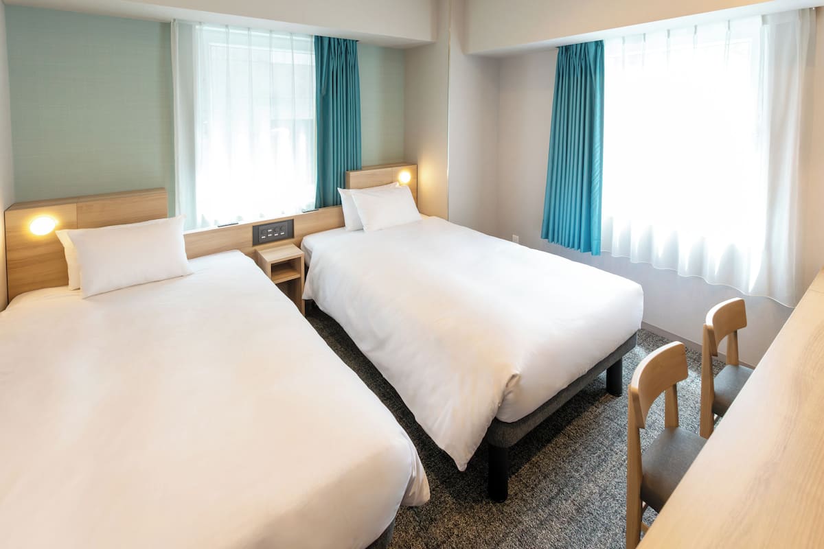 A hotel room with two beds, a desk, and a chair.