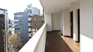 Un pasillo con suelo de madera, paredes blancas y un balcón con vistas a un paisaje urbano de edificios modernos.